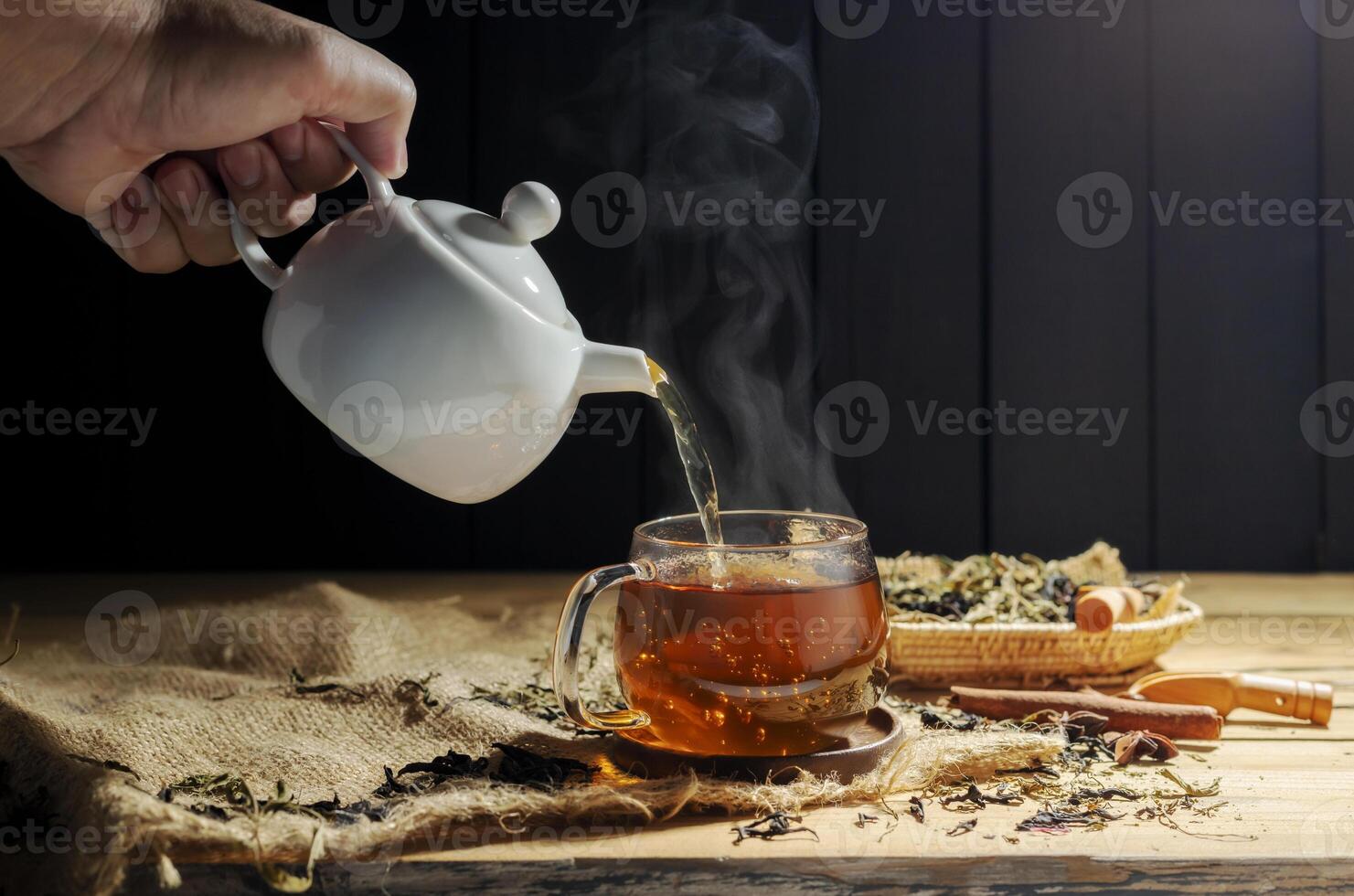 Pour hot tea into cups, herbal tea glasses are arranged on a rustic wooden table. photo