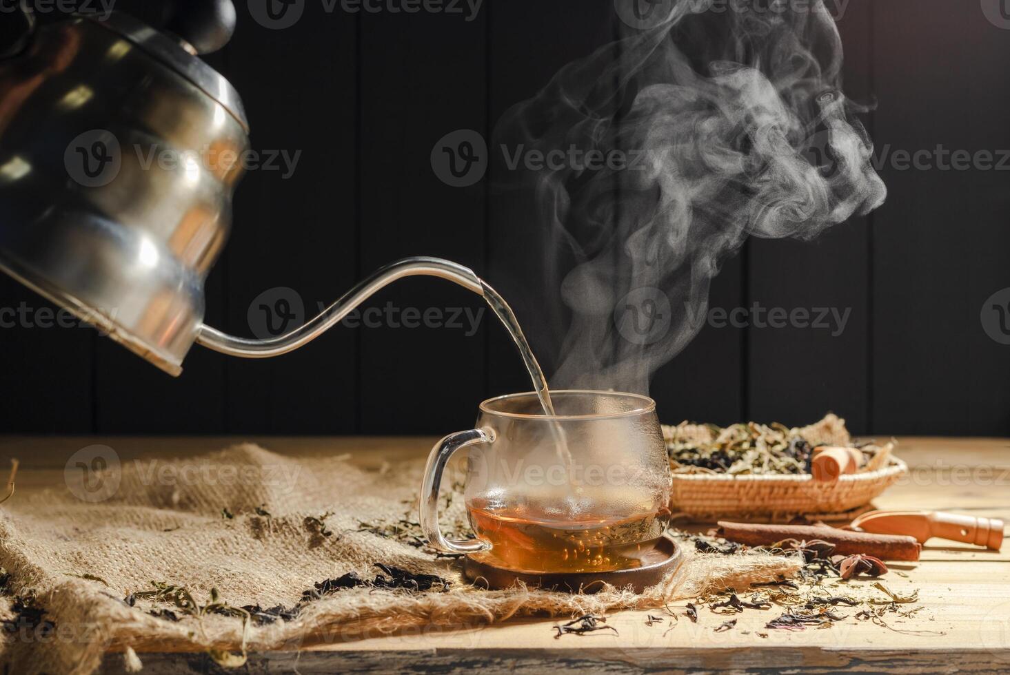Pour hot tea into cups, herbal tea glasses are arranged on a rustic wooden table.. photo