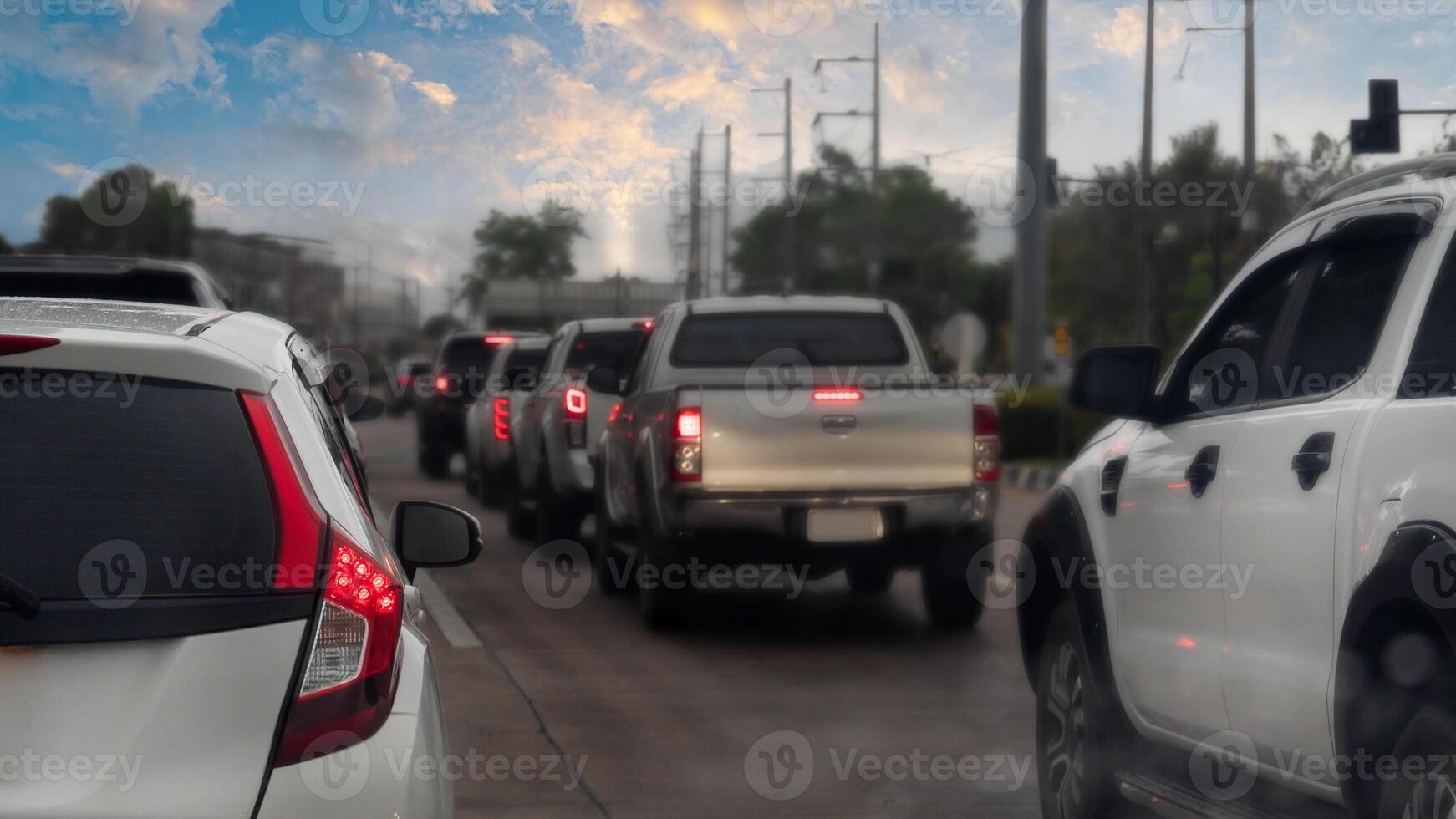 Traffic jam on the concrete road after rainy. Rear side of white car with turn on brake light. On car boy with drop of water rain. Many car in parked in a double row of tires. Environment in evening. photo