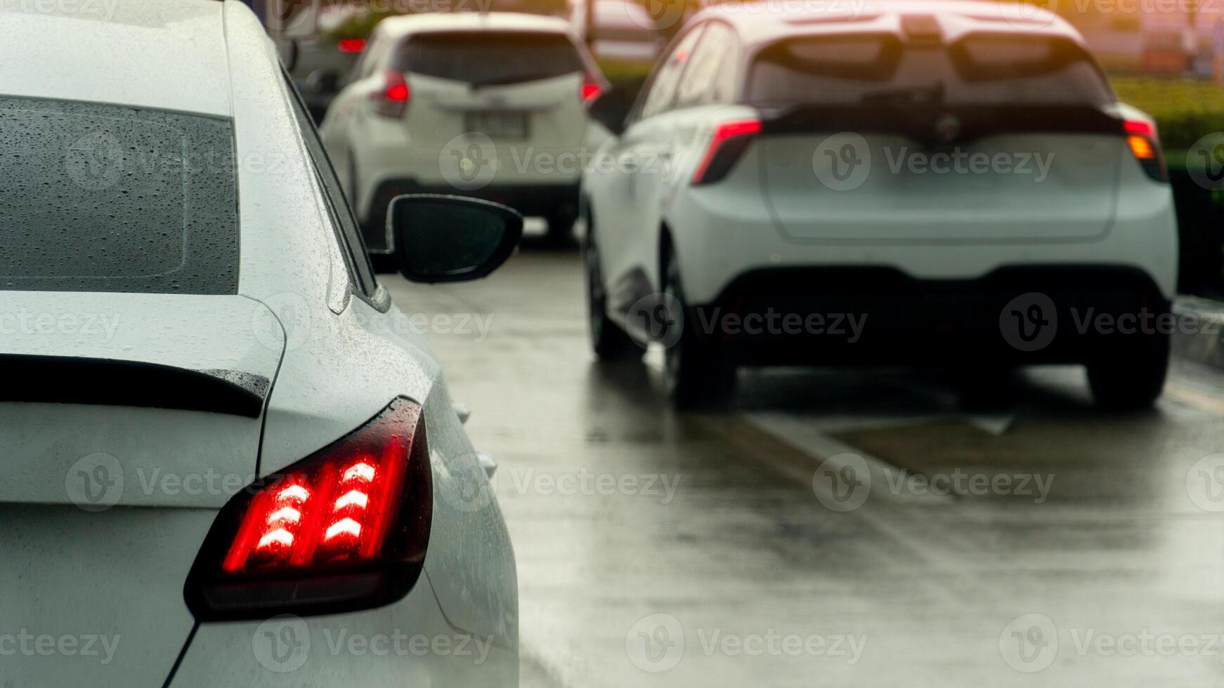 Rear side of white car on the car with wet from water rain. Turn on brake signal on the wet concrete road. Many car queue and stop on the road by trffic condition. photo