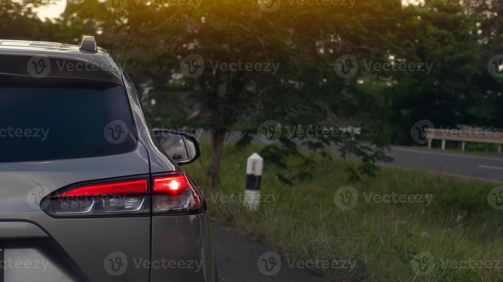 Luxury of grey car open light brake on the asphalt road. side road with trees and grass. On the opposite side is an empty road. photo