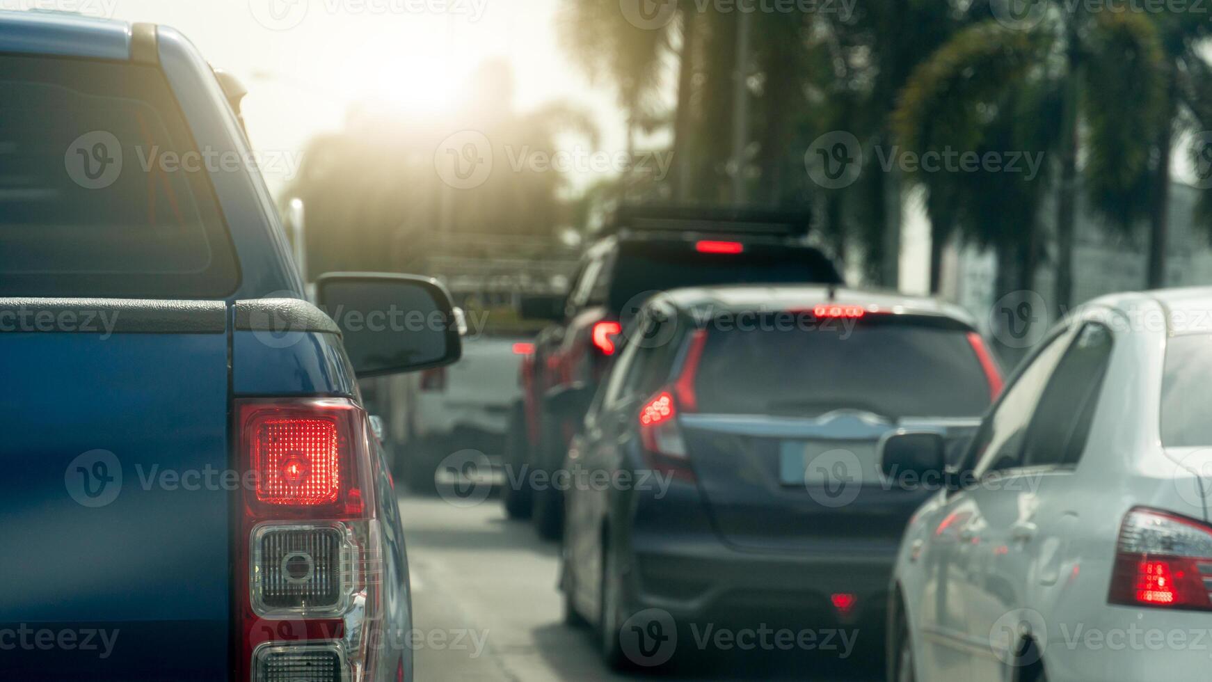 Rear side of blue pickup car with turn on brake light. Many car queue up due to traffic congestion. Side road with trees. Background of bright light of the sun shines. photo