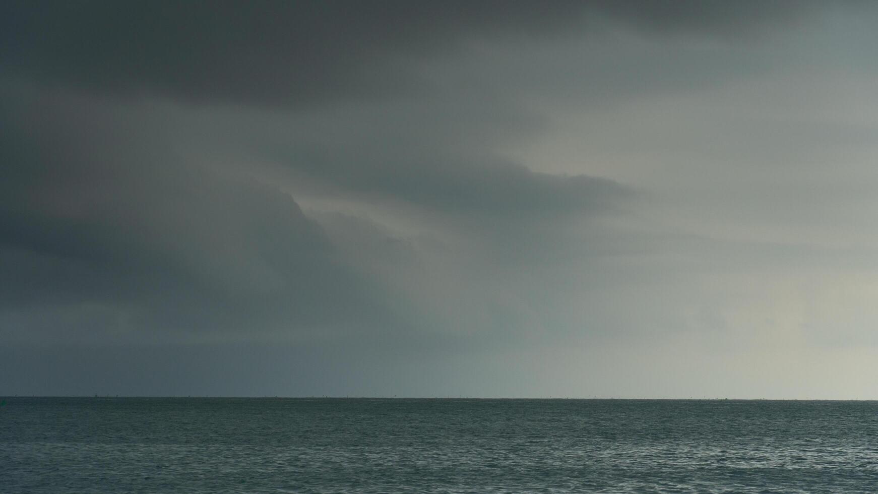 Vast expanse blue water of ocean under a cloudy overcast sky. Horizon line is visible with faint landmasses in the distance. The scene is moody and atmospheric before heavy rain. photo