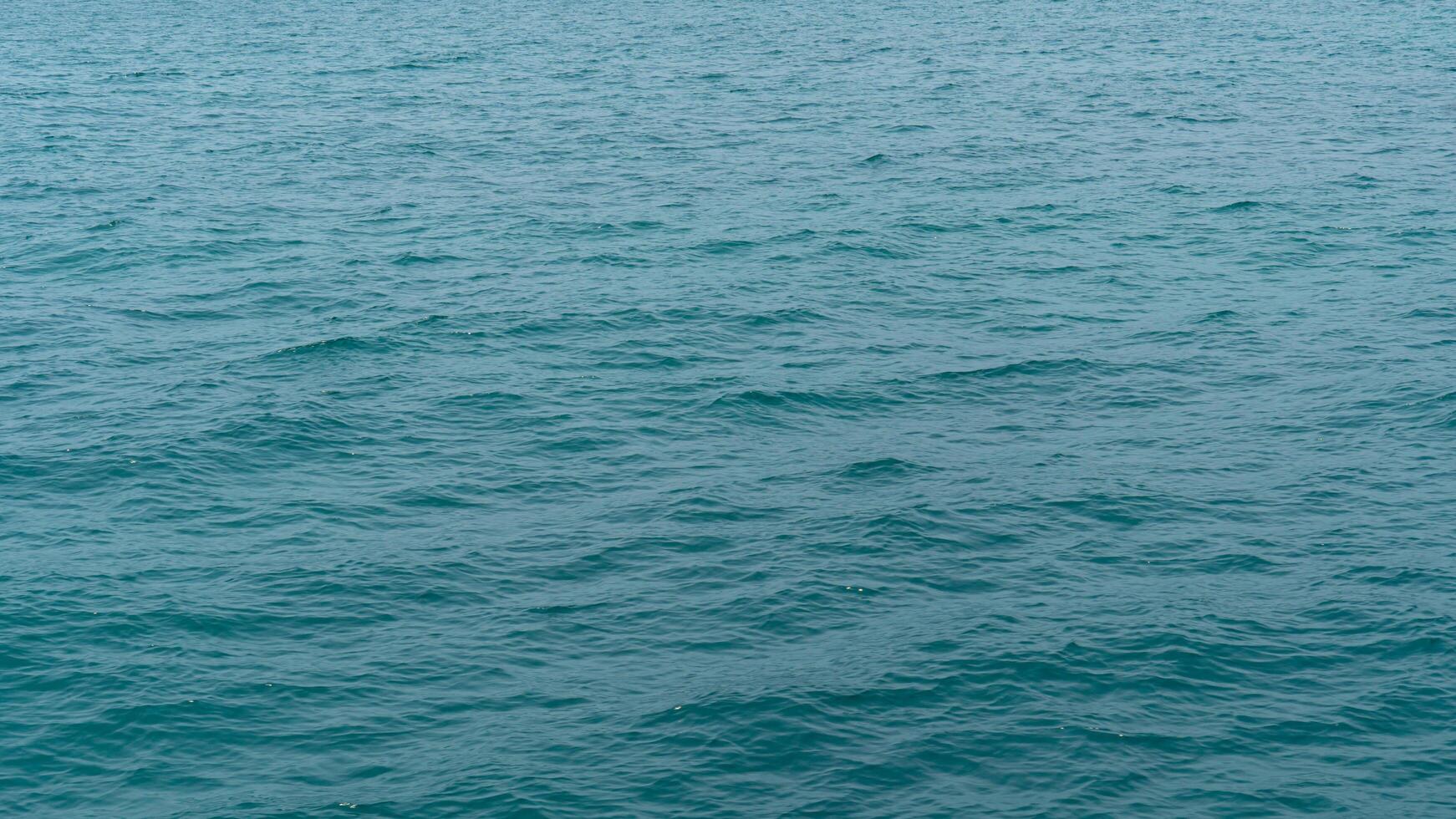 Water of ocean with gentle ripples. Water appears to be a consistent teal or blue green color suggesting a sea or large body of water. Focus is on the water texture and subtle movement. photo
