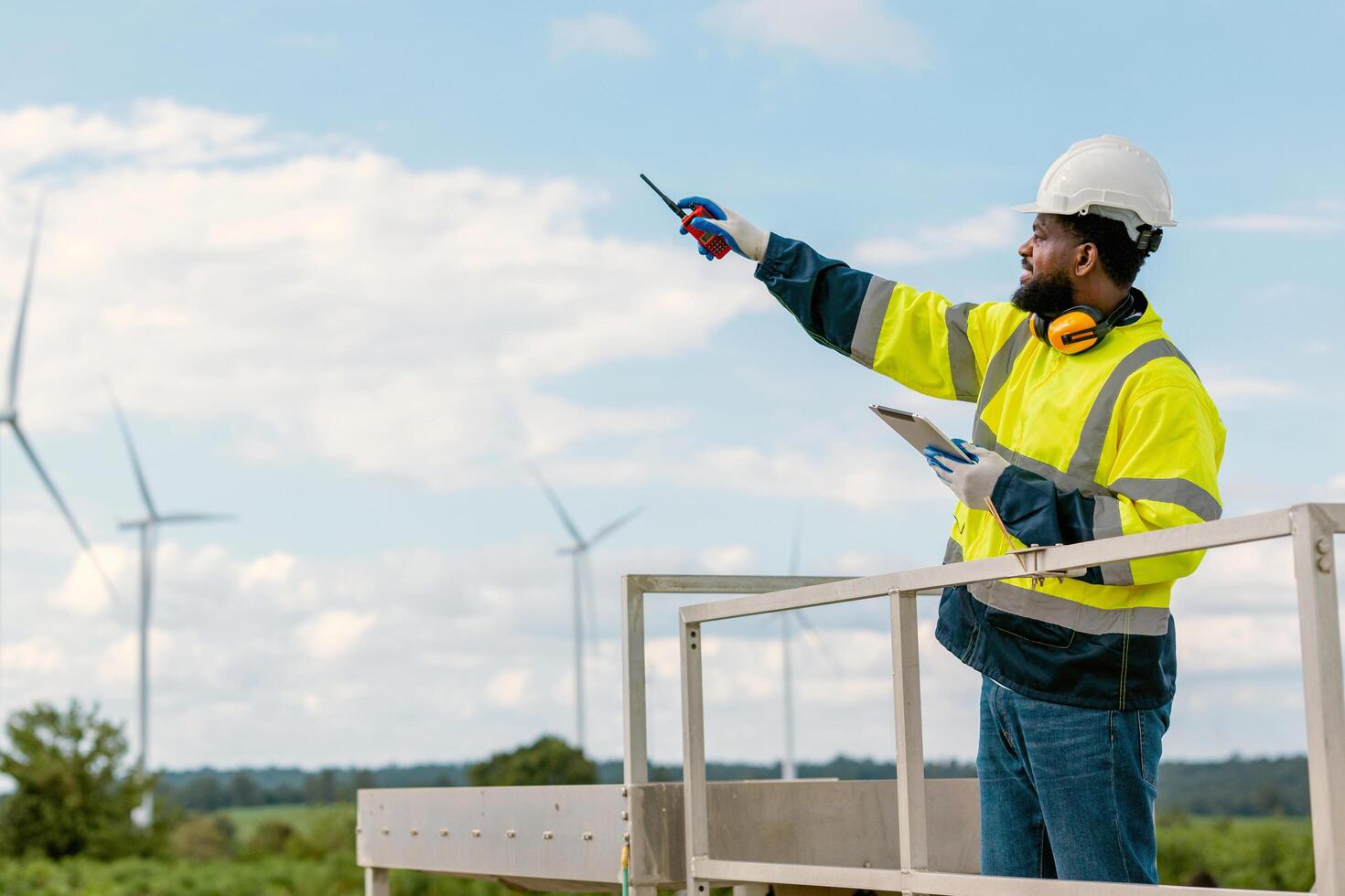 man in yellow and black safety vest is pointing at a wind turbine photo