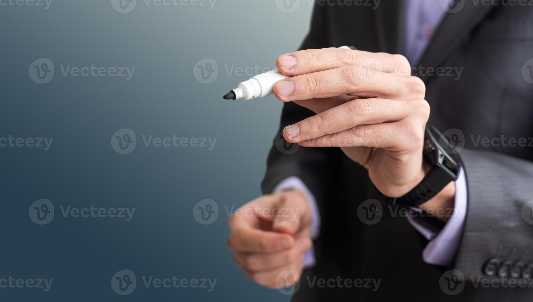 Man writes something on screen. Businessman raised his hand to screen. Concept - businessman writes on a virtual screen. Businessman held out a pen to camera. Guy in a dell suit on black background. photo