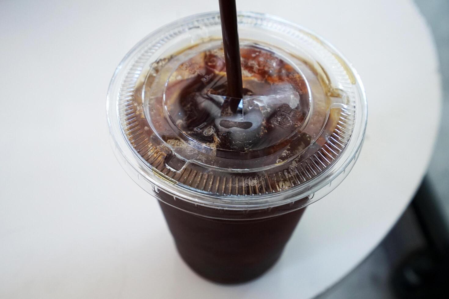 Close up plastic take away cup of iced black Americano coffee on white table photo