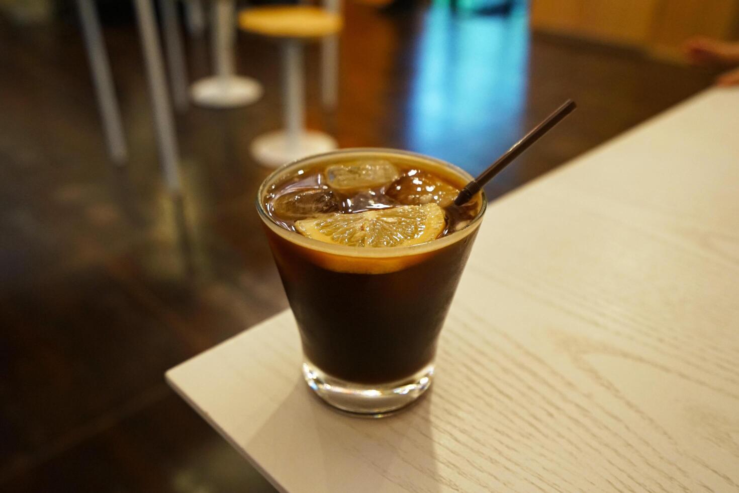 Close up glass of iced black coffee with sliced of lemon on wooden table photo