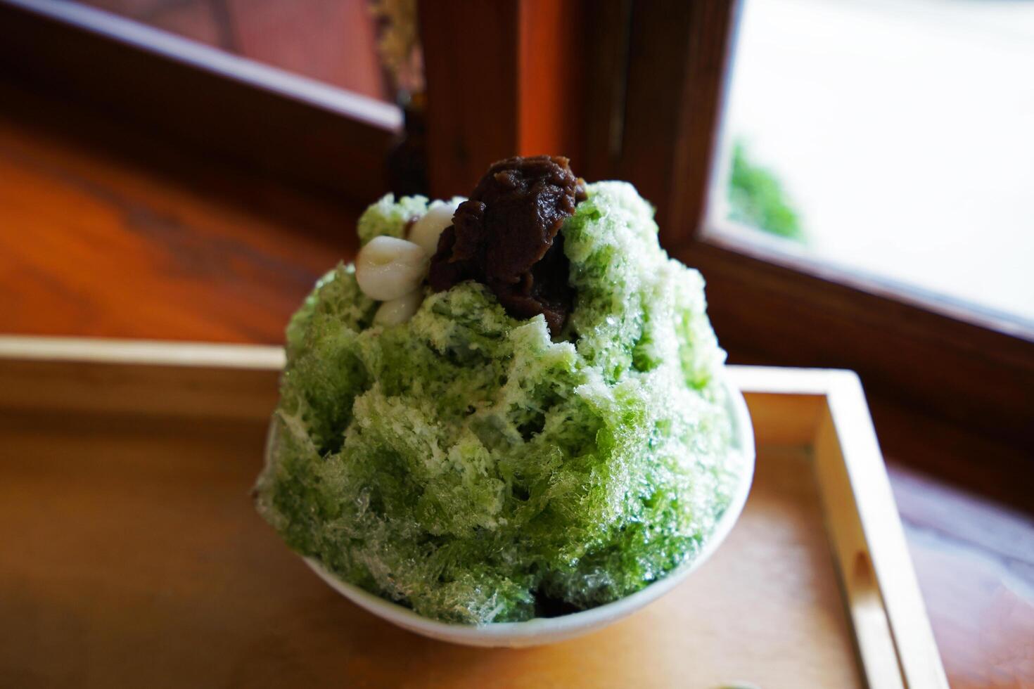 Close up Matcha green tea Kakigori topped with mochi and mashed red beans on wooden tray table, Japanese shaved iced dessert photo