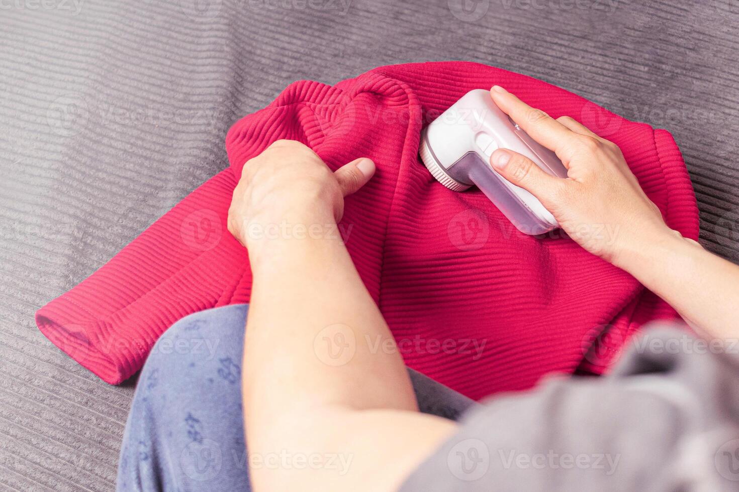 Woman uses a machine for removing pellet from clothes . Electronic device for updating old things close up photo. Pink red jacket photo