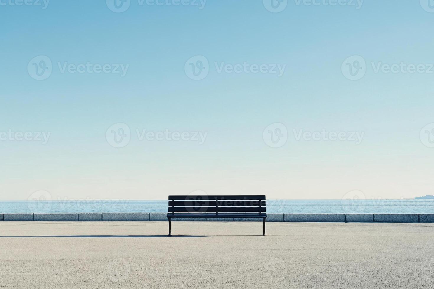 A solitary bench facing the calm sea under a clear blue sky. photo