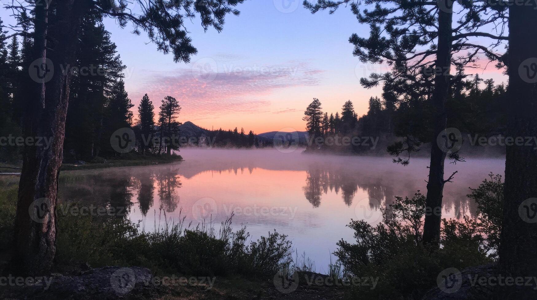 Serene lake at dawn with mist and trees reflecting a colorful sky. photo