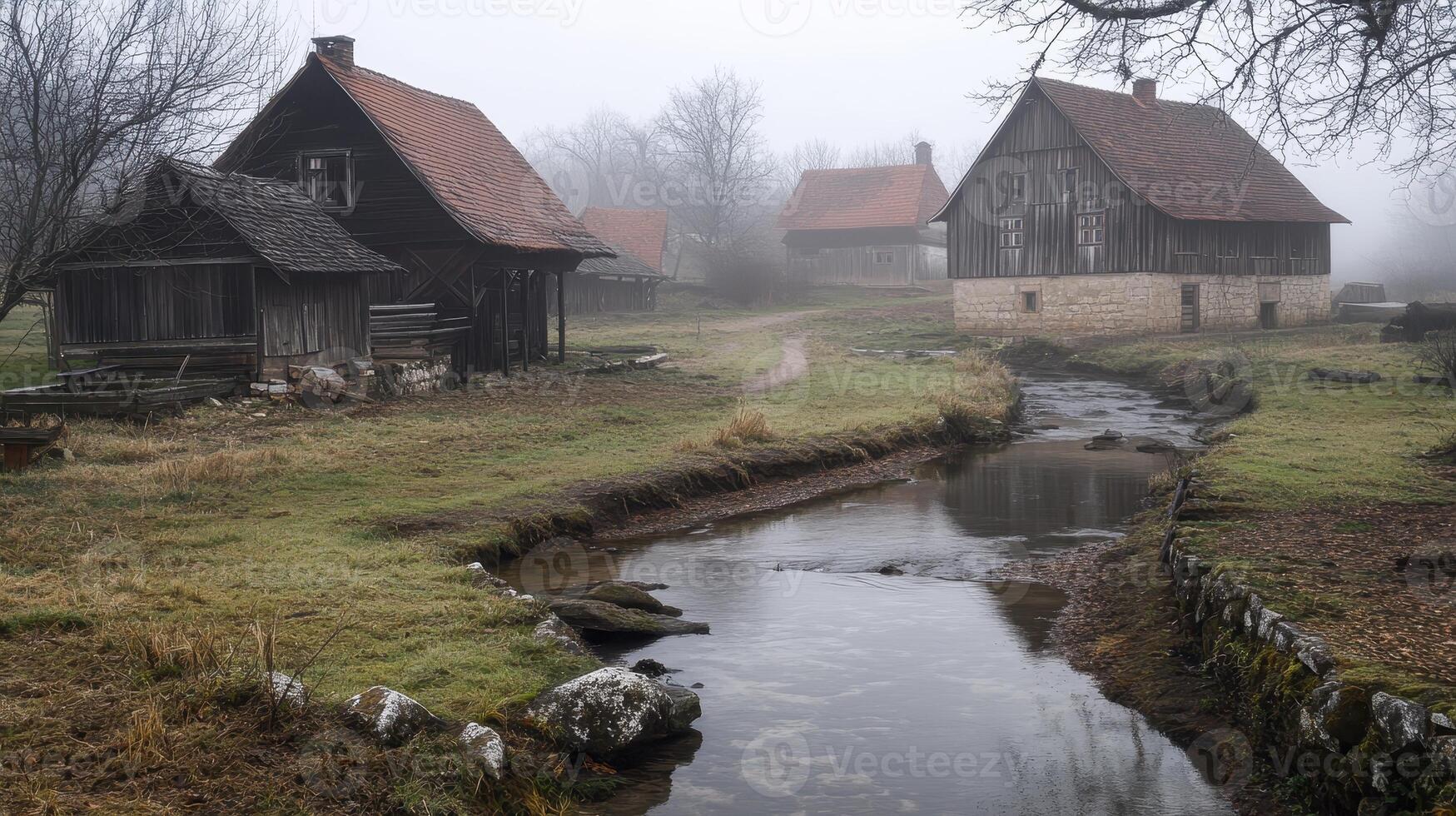 A serene foggy landscape featuring rustic houses beside a gentle stream. photo
