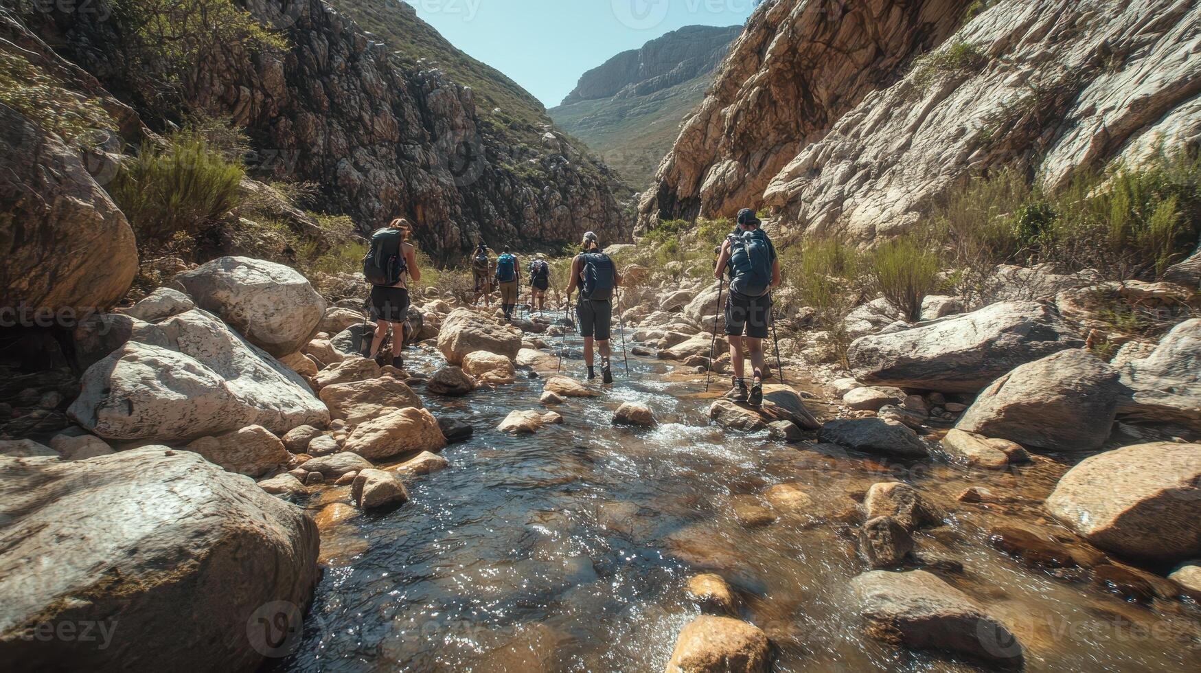 A group of hikers trekking through a rocky stream in a mountainous landscape. photo