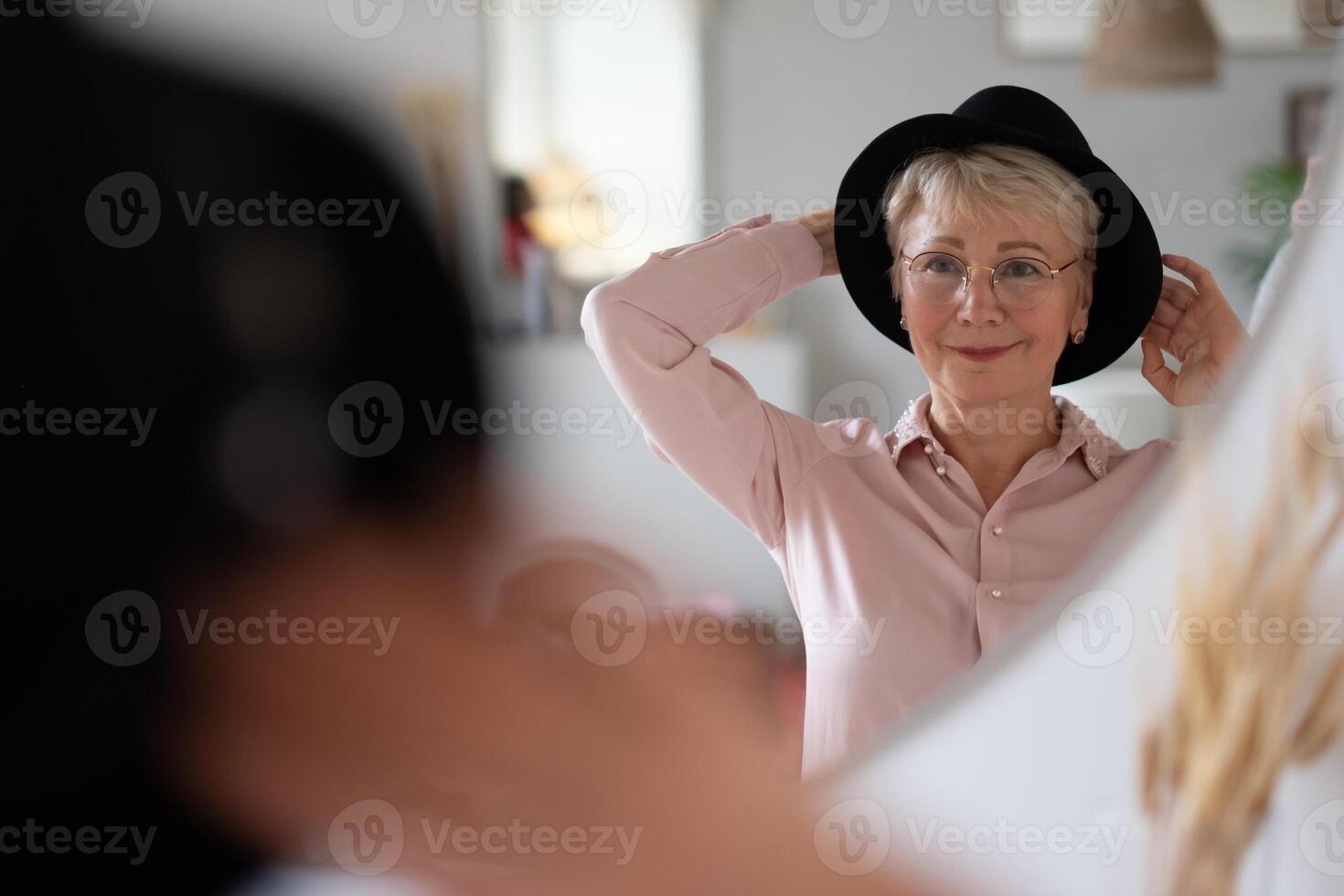 Caucasian woman trying on hat looking in mirror at home preparing for walk. photo