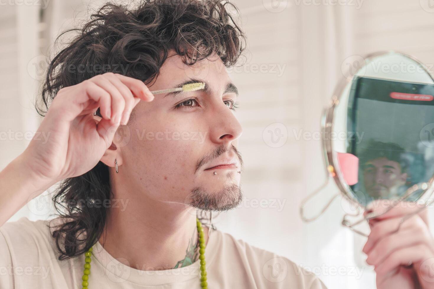 Young man combing eyebrows with a small brush and mirror in bathroom photo