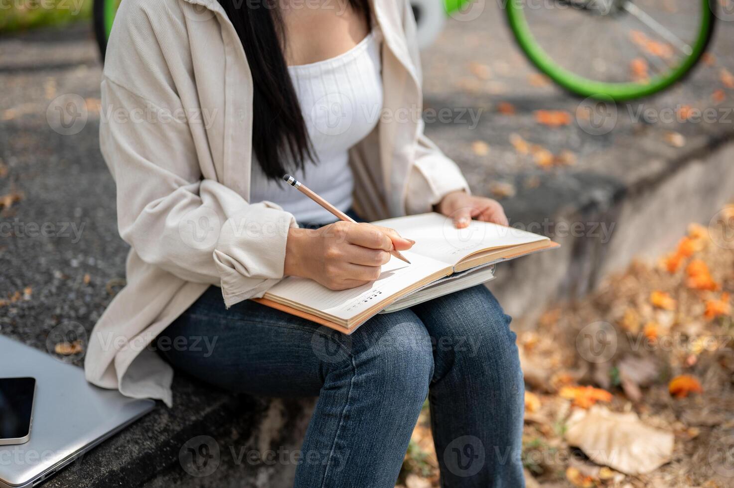 A close up of woman sitting on the side walk, writing or drawing in the notebook. Outdoor activity. photo