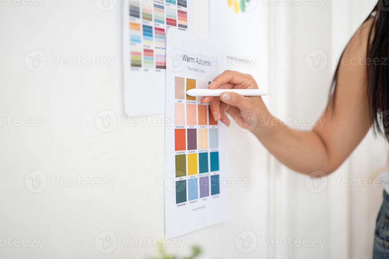 Close up of hand holding a stylus pointing at a color on printed color palette sticking on the wall photo