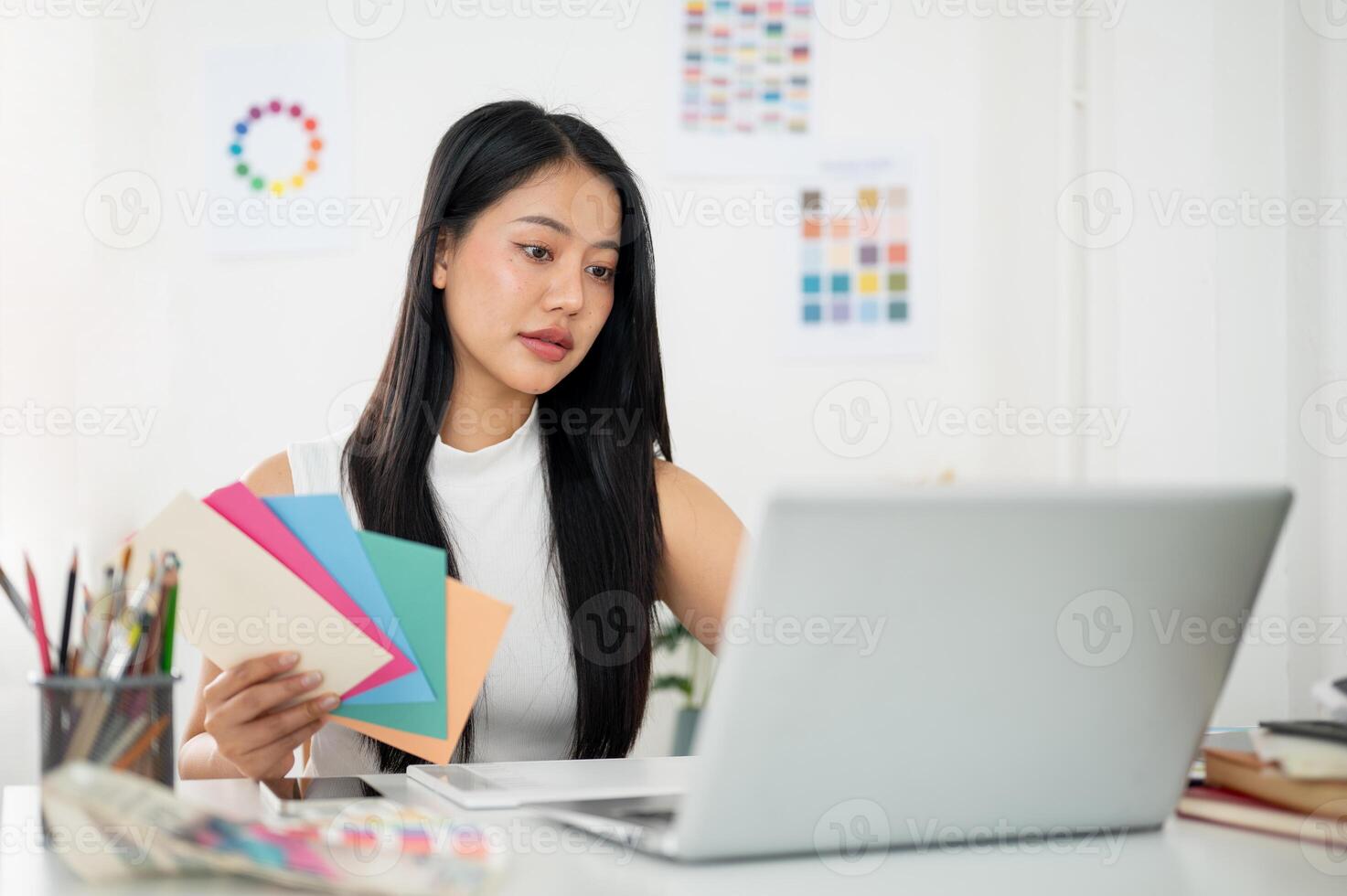 Asian woman is working on the design in laptop with selected colors from paper color charts. photo