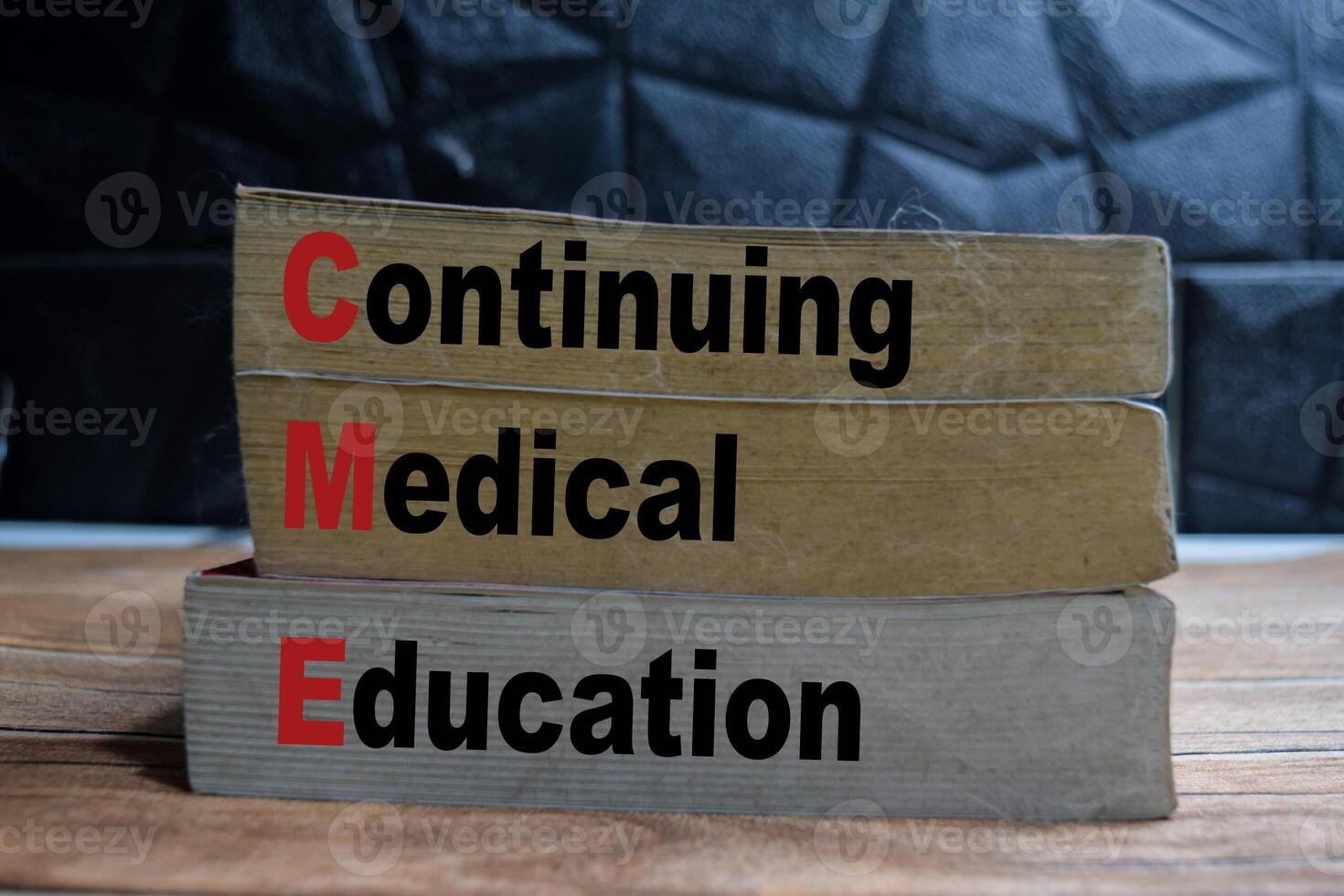 Books with words CME - Continuing Medical Education on wooden table and black background photo