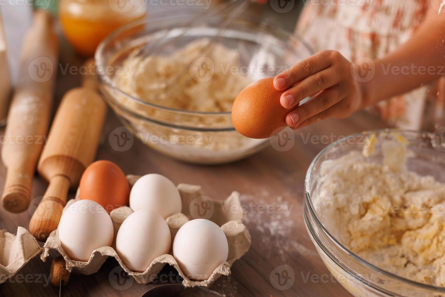 Kid baking with eggs, dough, and kitchen tools on a rustic wooden table. photo