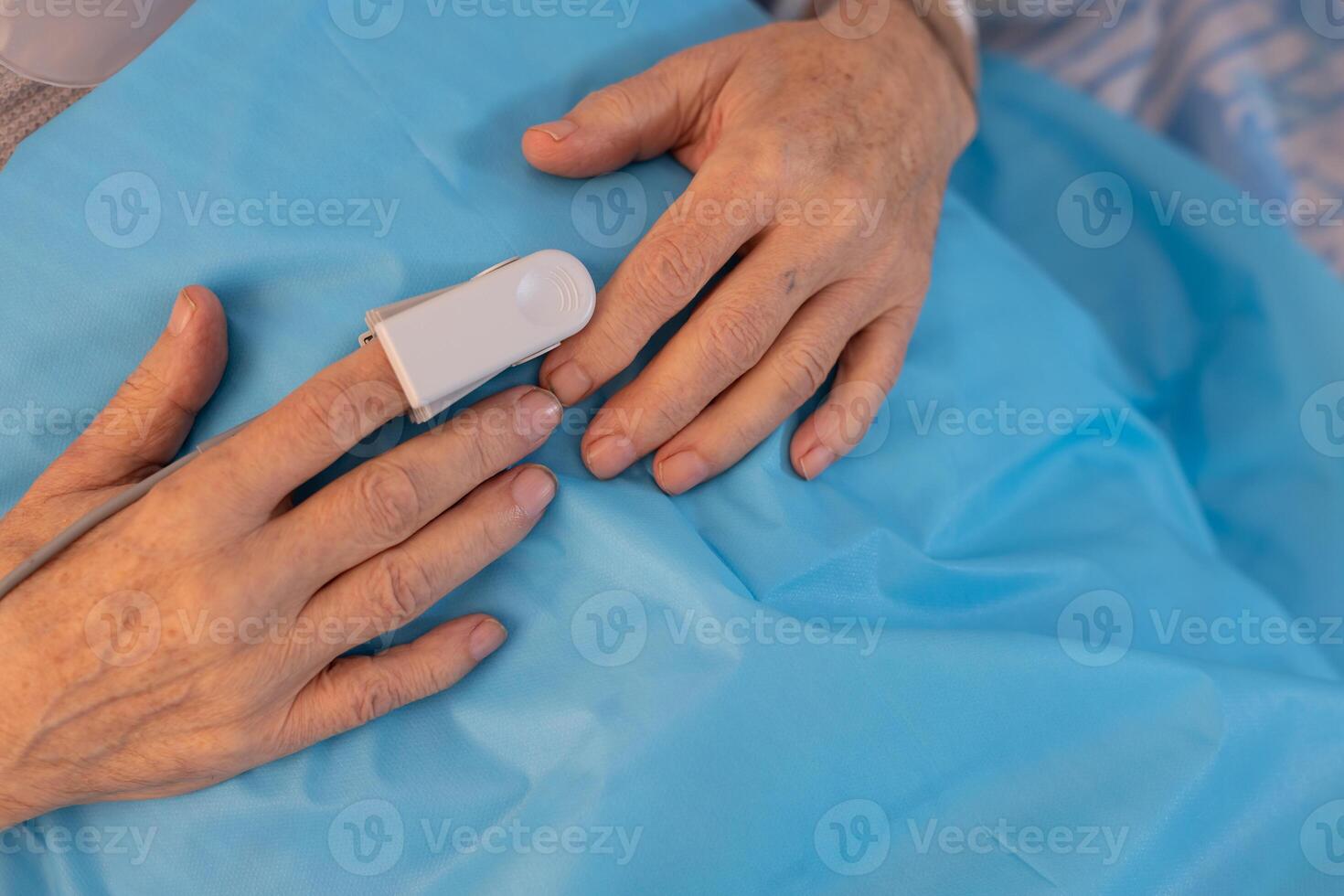 Senior hand with pulse oximeter on blue hospital sheet, monitoring oxygen saturation. photo