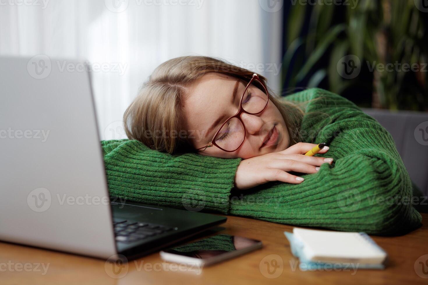 Woman sleeping on desk next to laptop and notepad, exhausted from work or study session. photo