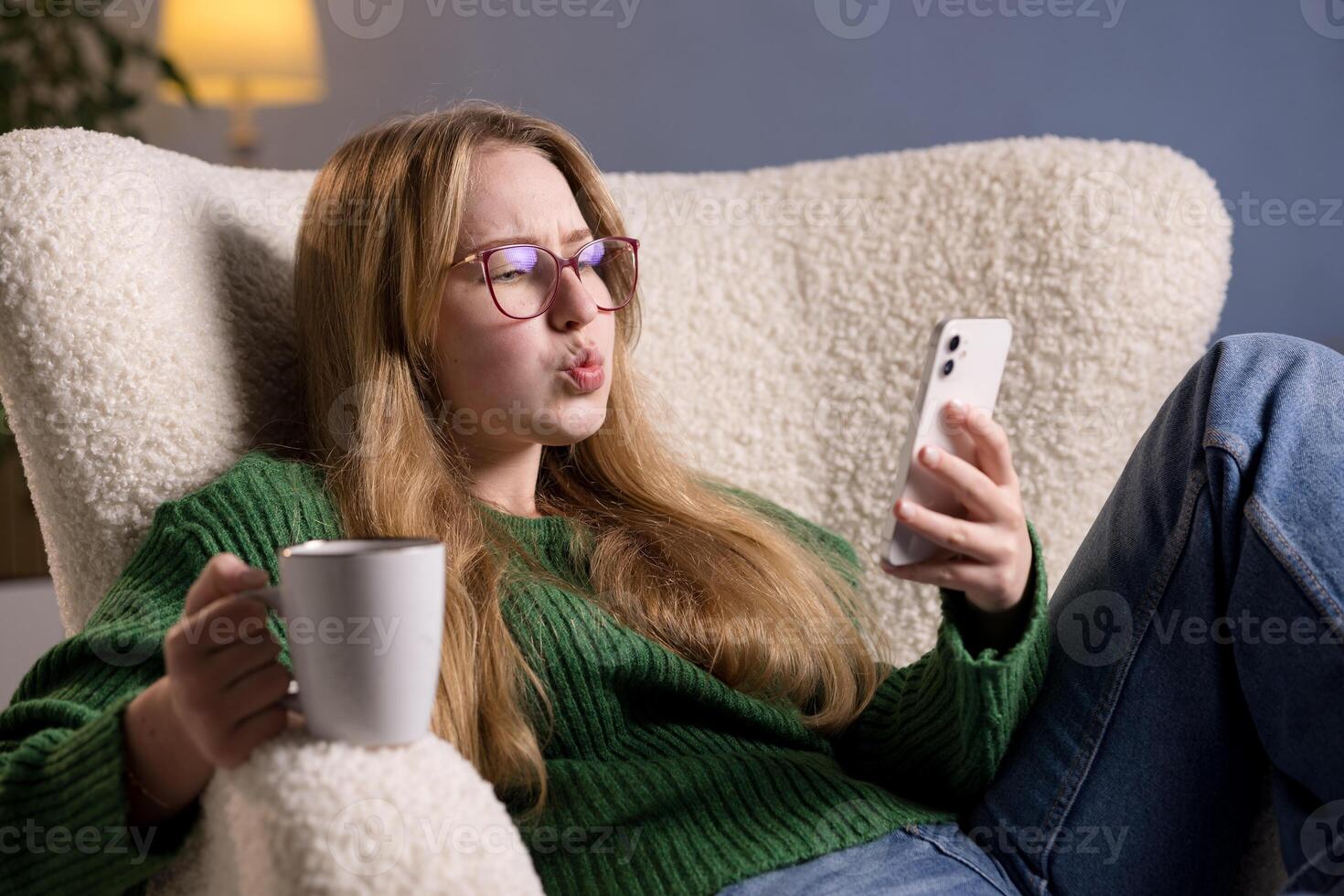 Woman with coffee and smartphone shows surprised expression while reading something online at home. photo