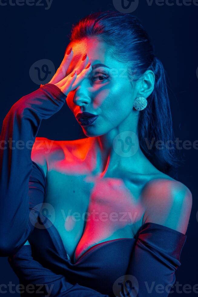 Close-up of stylish woman in dramatic colored light, posing with intensity and elegance. photo