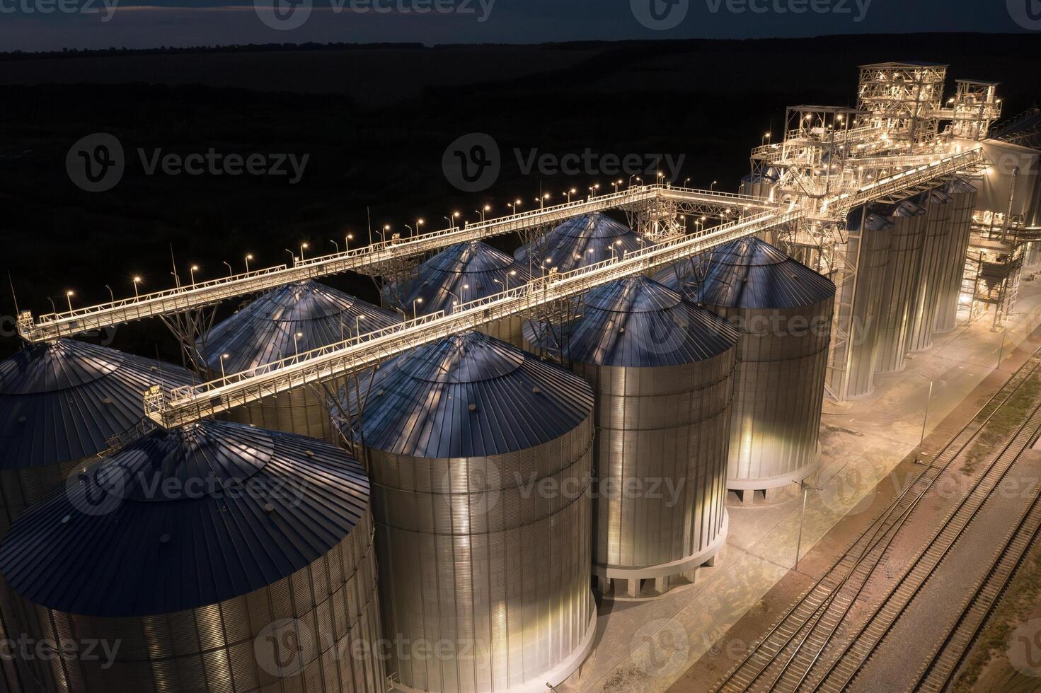 Grain silos and elevator complex glowing at night, aerial view of agricultural industry, agricultural technologies photo