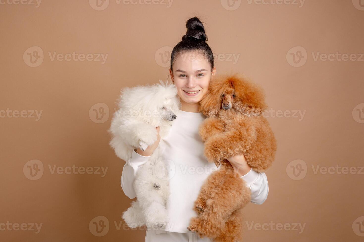 Happy woman in white clothes holding two fluffy poodles in studio with neutral background. photo
