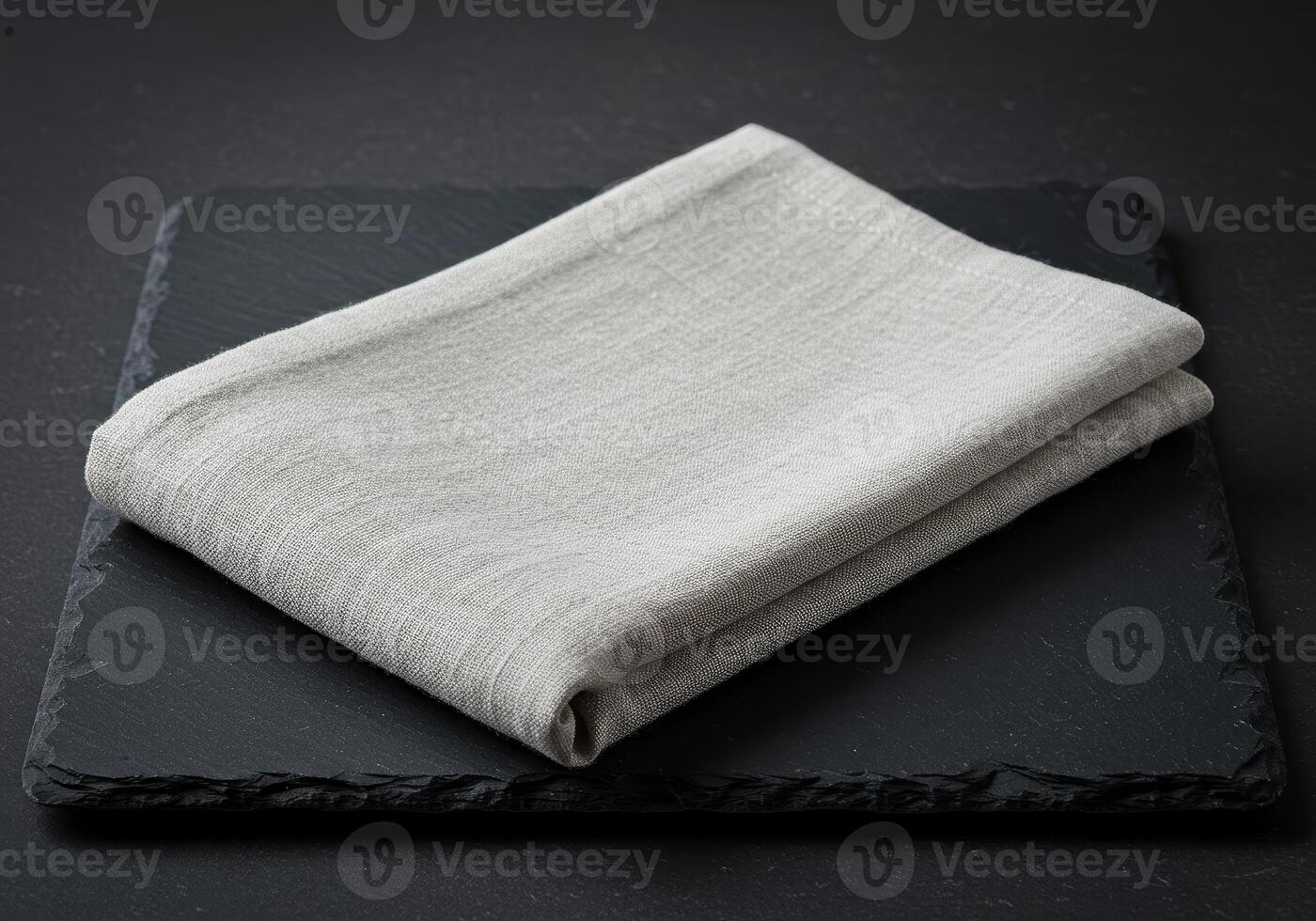 Beige folded linen fabric on dark slate surface with natural textile texture in minimal neutral style flatlay closeup for background or design use photo