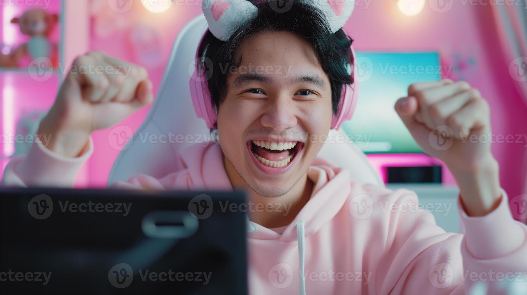 Cheerful asian gamer winning match in pink gaming room portrait image. Kawaii male geek nerd cat-ears headphones photography human scene. Esport content creator concept photo-realistic photo