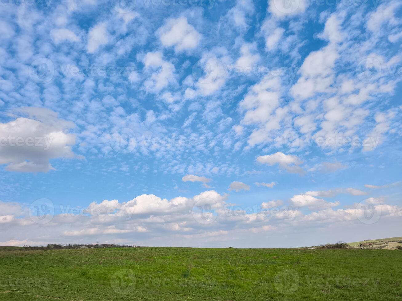 Verdant rolling hill rising against soft altocumulus clouds spreading across expansive azure sky background photo