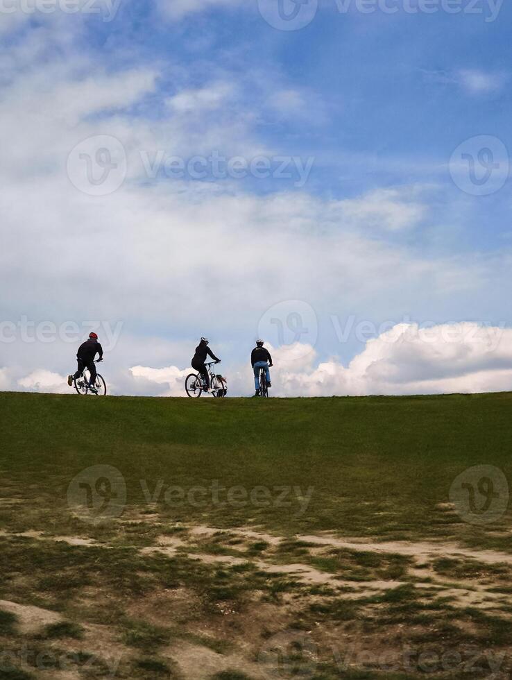 Cyclists pedaling uphill on verdant meadow, embracing fitness challenge beneath overcast sky with scenic mountain landscape photo