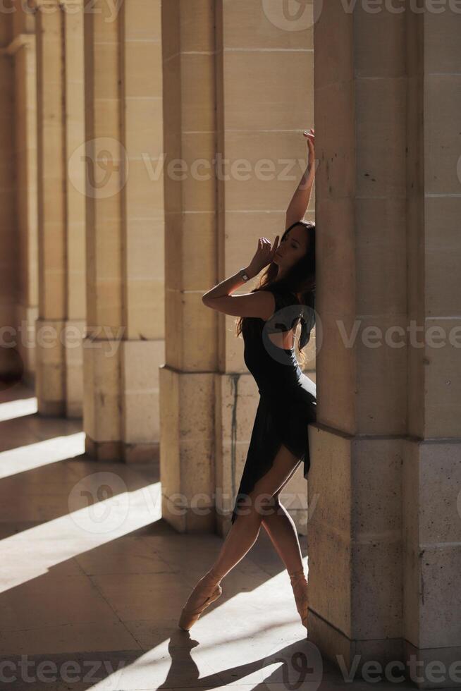 Ballet dancer striking elegant pose in stone arcade. Soft directional lighting photo