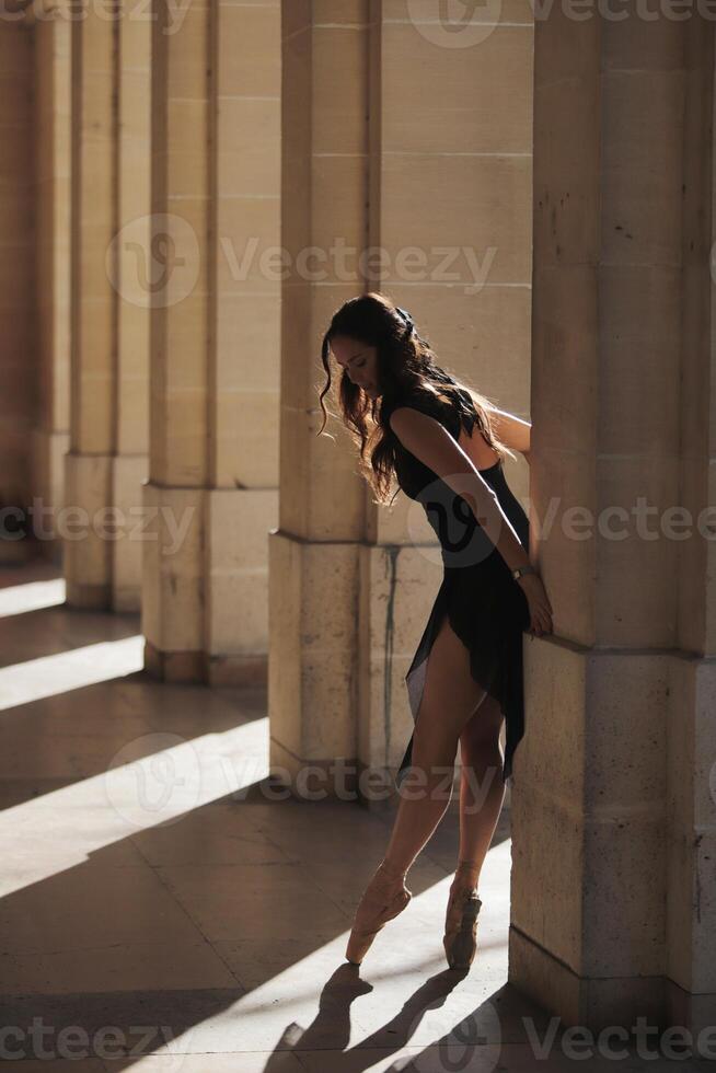 Ballet dancer en pointe leaning gently on column in sunlit stone corridor photo