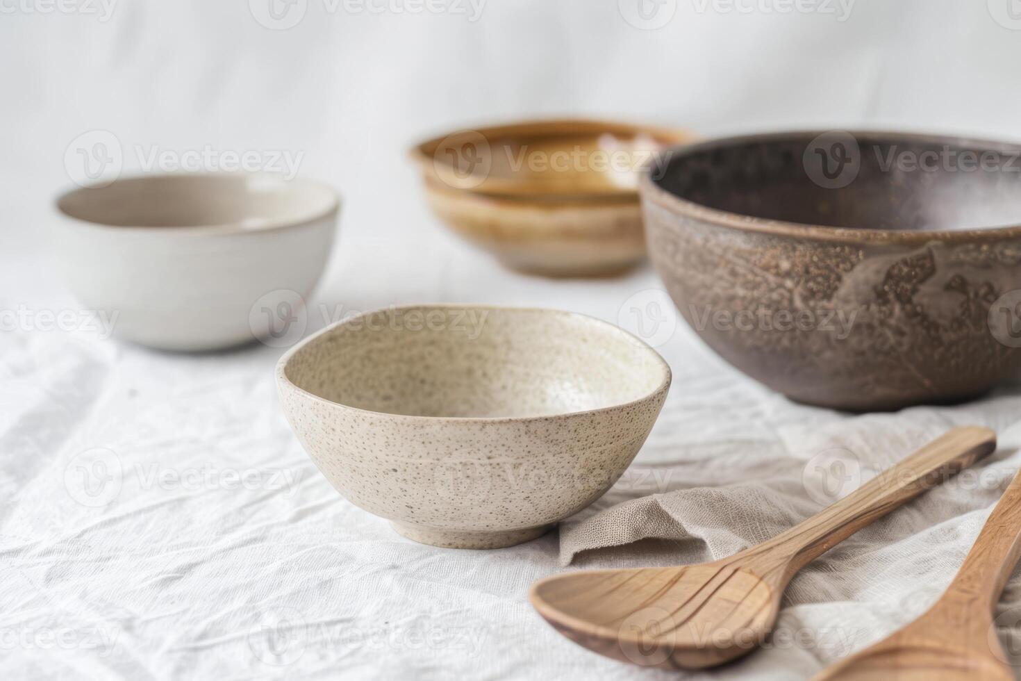 Colorful ceramic bowls of different sizes rest on a textured surface with wooden utensils photo