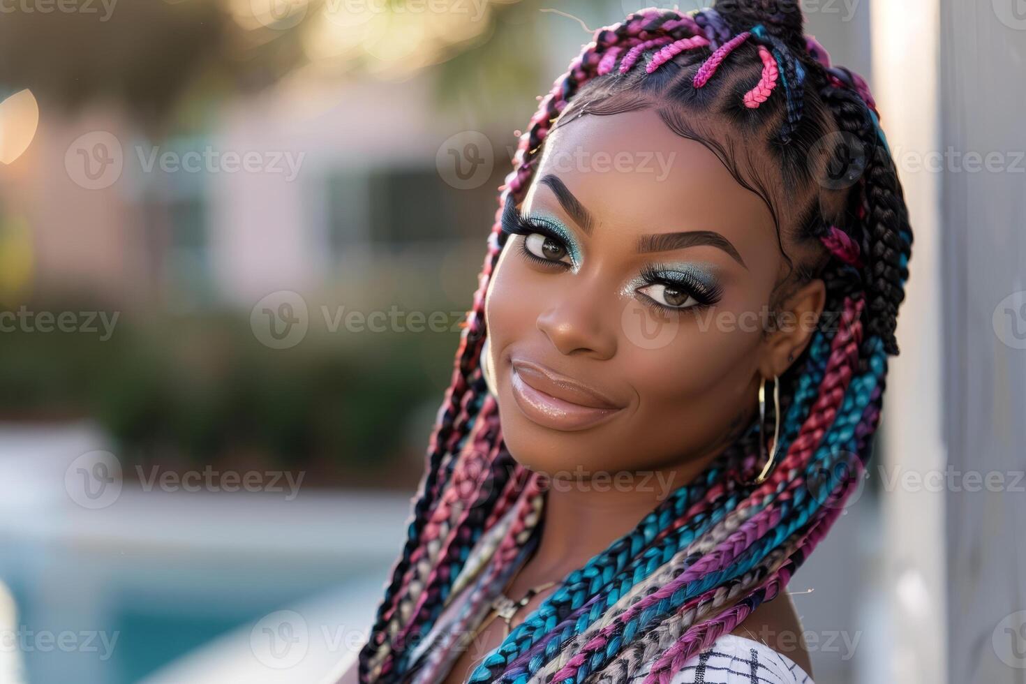 Brightly lit, a Black woman with long, vibrant braids showcases her stunning look while smiling in an outdoor setting filled with greenery photo
