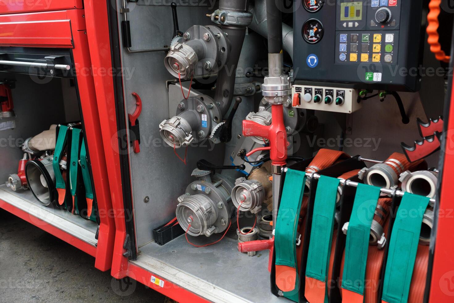 Equipment used for firefighting is neatly organized in a fire truck compartment with hoses, valves, and control panels present in the background during daylight hours photo