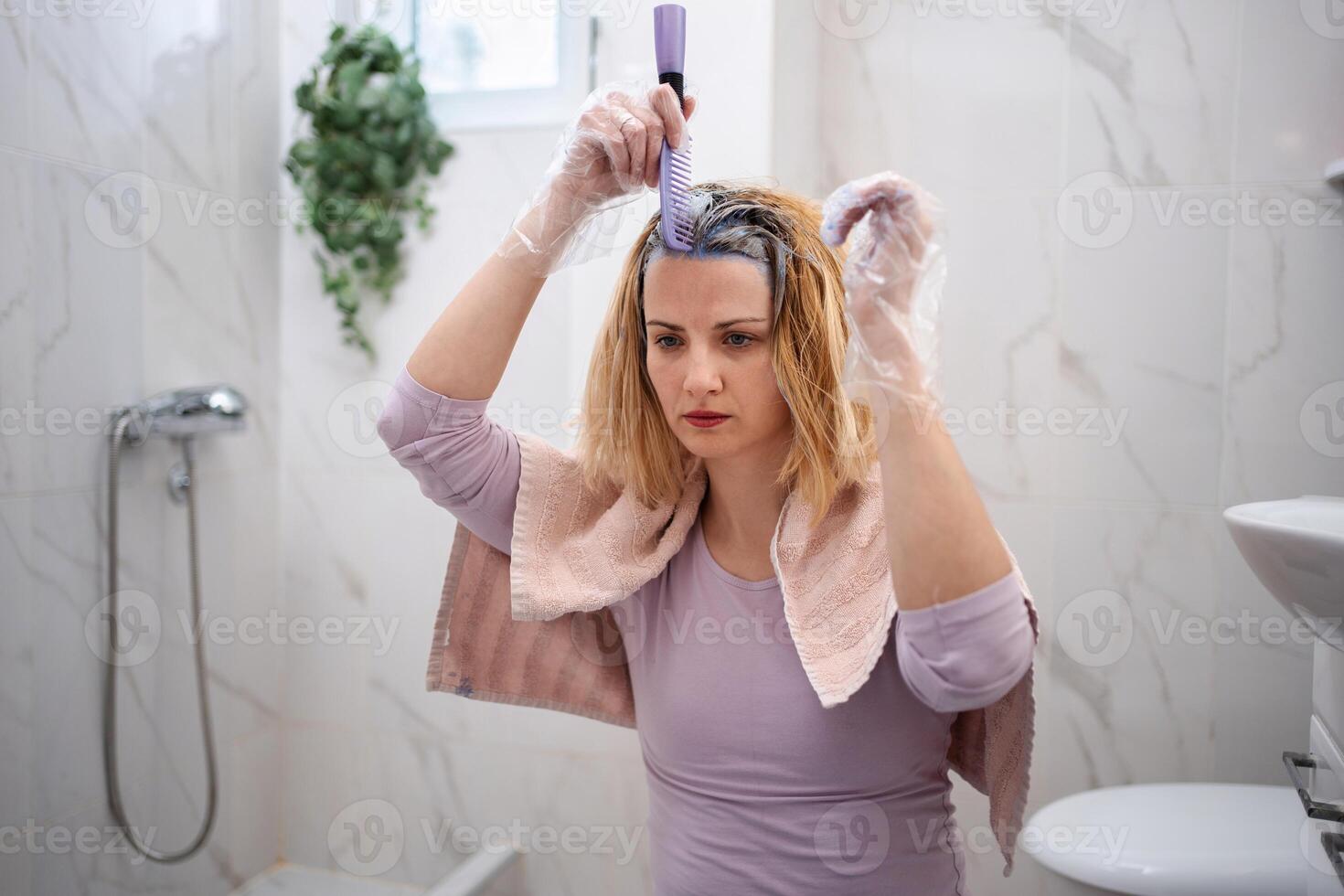 Woman dyeing her hair at home in the bathroom photo