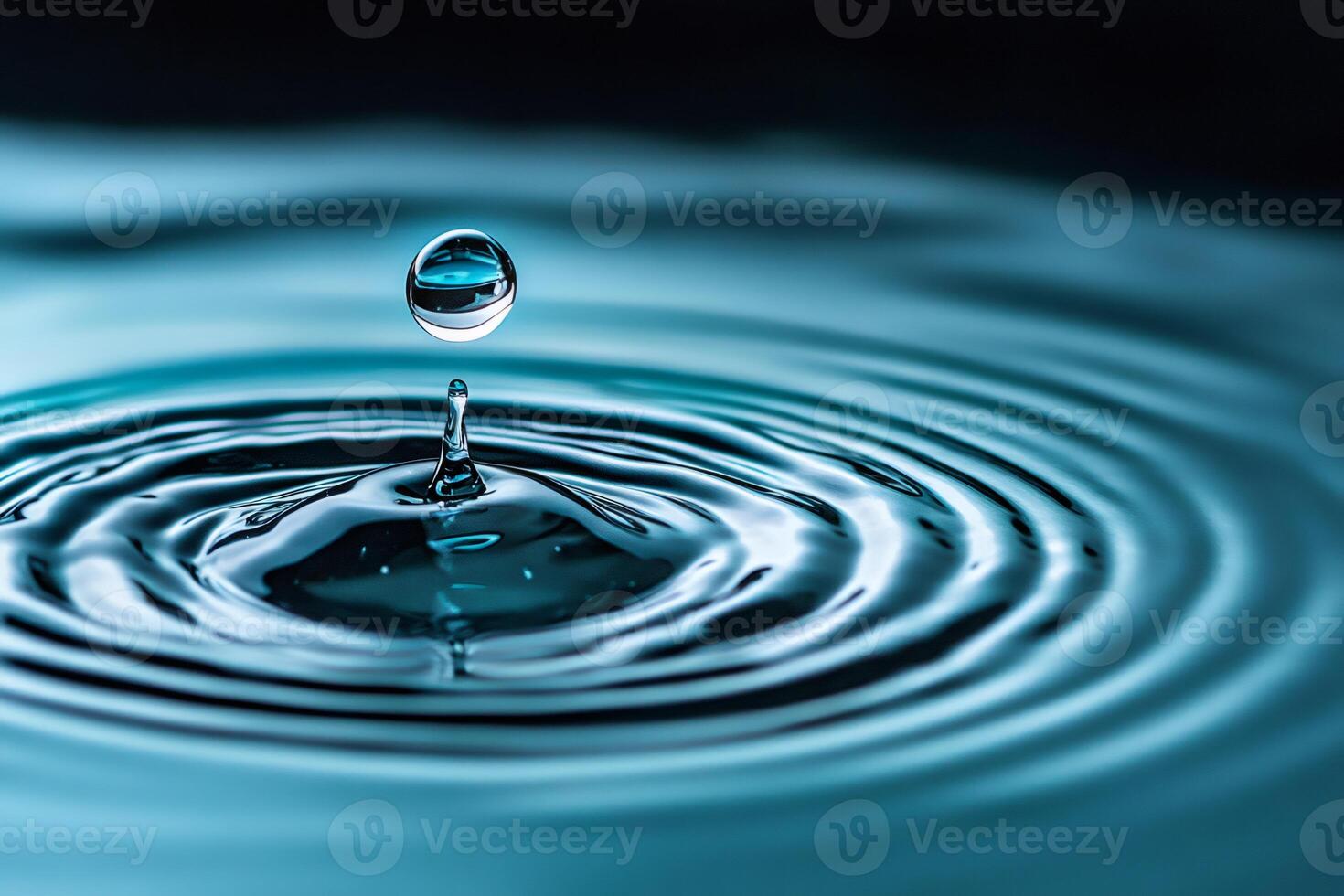 Water drop making ripple effect on blue liquid surface photo