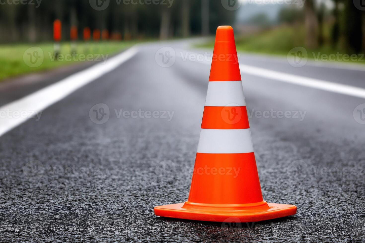 Orange traffic cone standing on asphalt road leading to forest photo