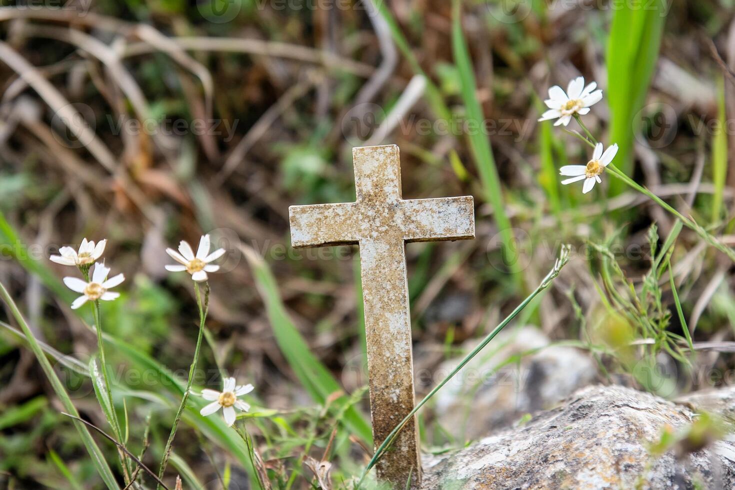 A cross is sitting on a rock in the grass photo