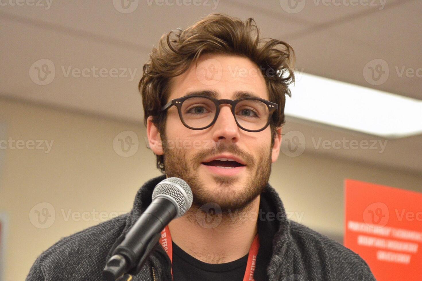 A man with glasses and a beard is speaking into a microphone photo
