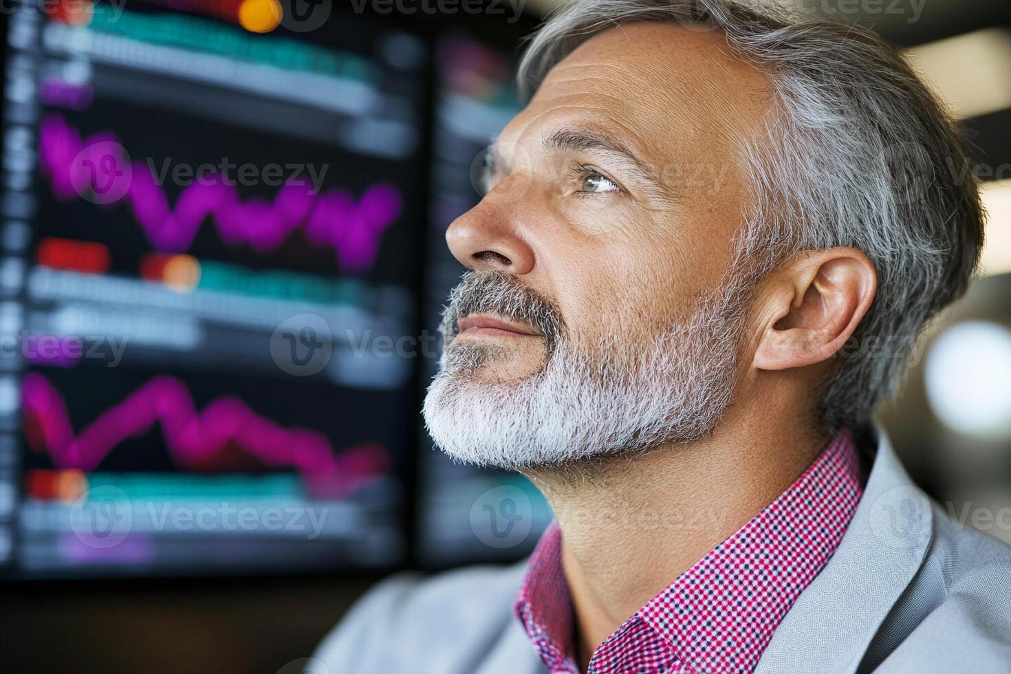 A man with a beard and a gray suit is looking at a screen photo