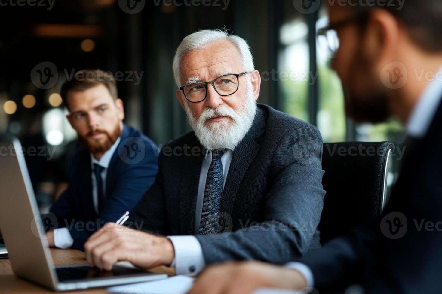 An older man with a beard and glasses sitting at a table with two other men photo