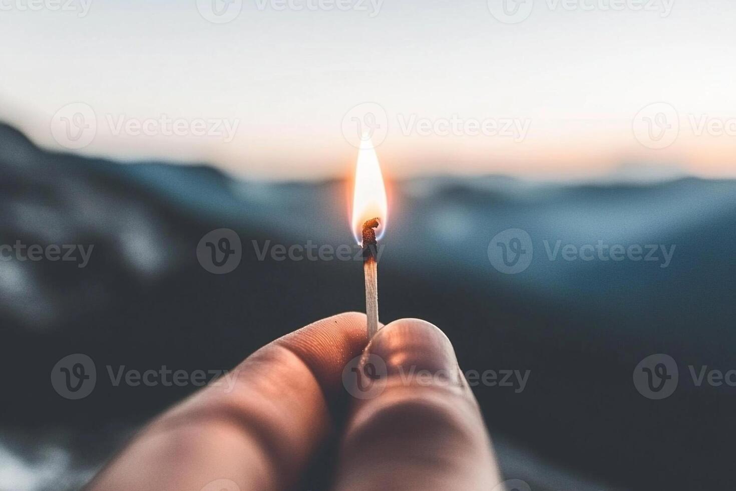 A person holding a lit match in front of a mountain photo
