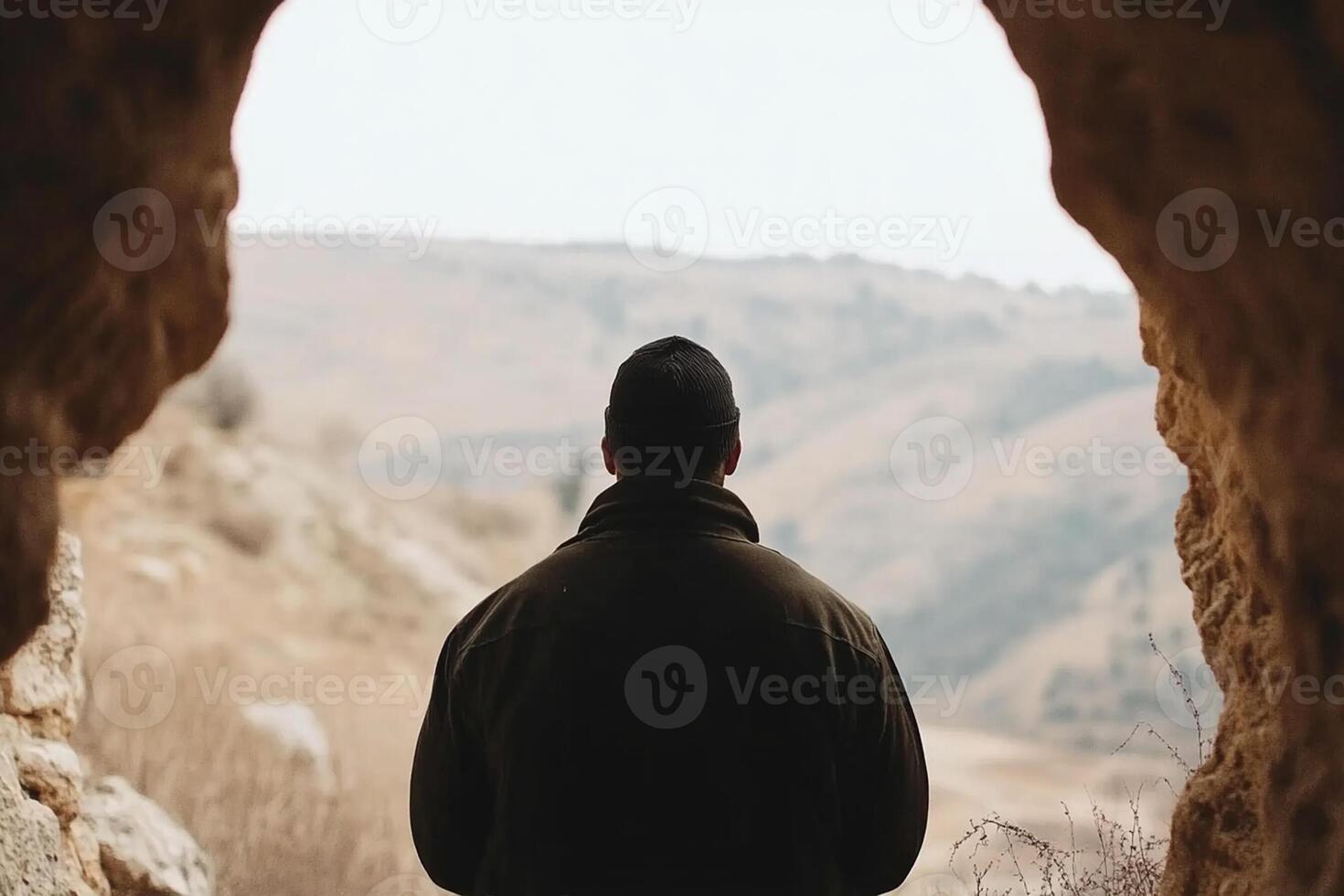 A man standing in a cave looking out over a valley photo