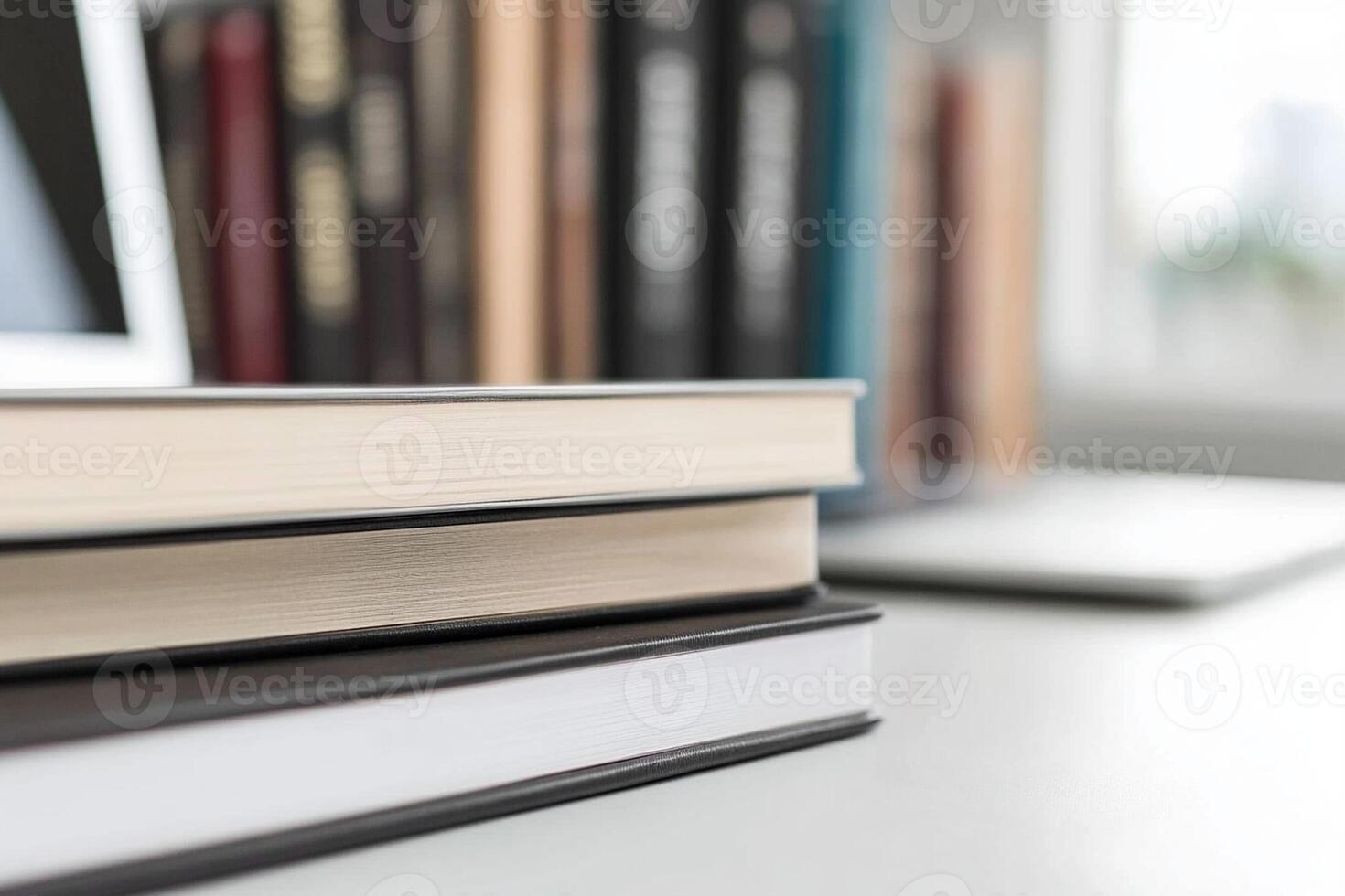 A stack of books on a desk next to a laptop photo